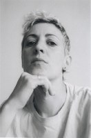 A gray-scale headshot photo of melaie frisoli wtih her right hand under her chin, head angled up, and eyes gazing downwards towards the camera. 