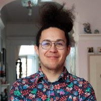 A photograph of Emmanuel Boucher wearing a flower pattern shirt indoors with a white archway and bright window in the background.